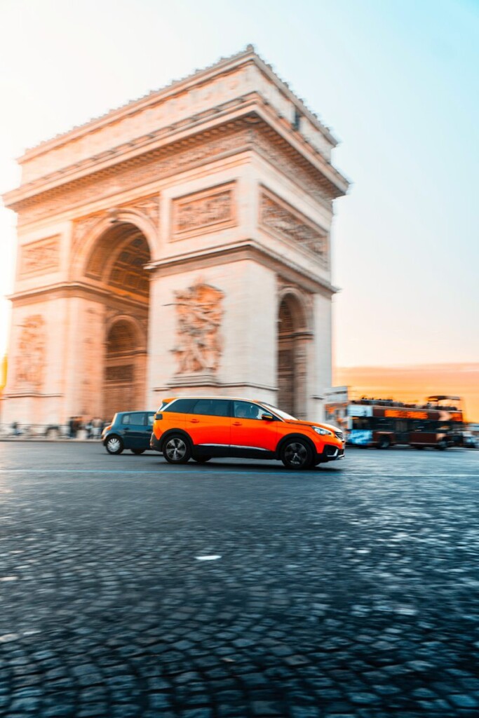 a small orange car driving past a tall building