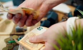 Hands counting euro banknotes with coins scattered around.