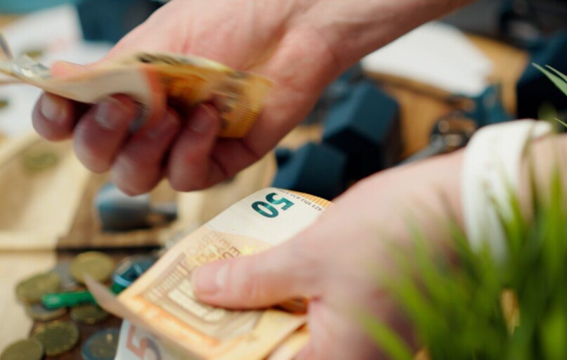 Hands counting euro banknotes with coins scattered around.