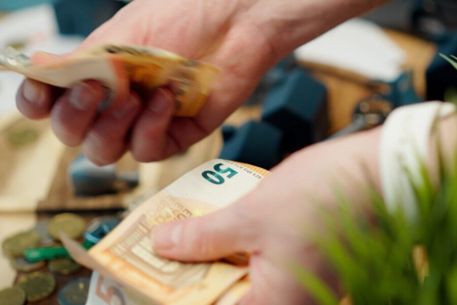 Hands counting euro banknotes with coins scattered around.