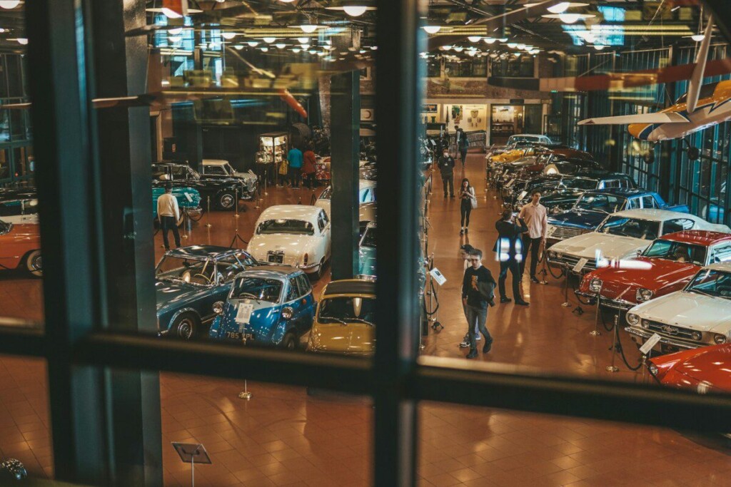 a group of people standing around a museum filled with cars