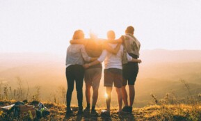 four person hands wrap around shoulders while looking at sunset