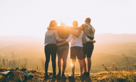 four person hands wrap around shoulders while looking at sunset