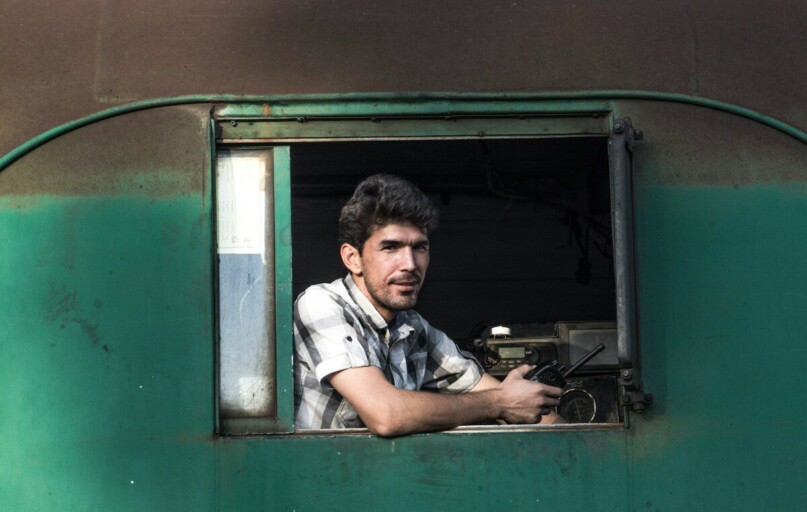 man in white and black plaid button up shirt sitting on green and black bus