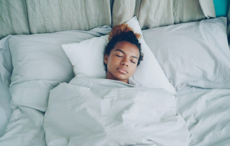 A young woman sleeping peacefully in a white bed.