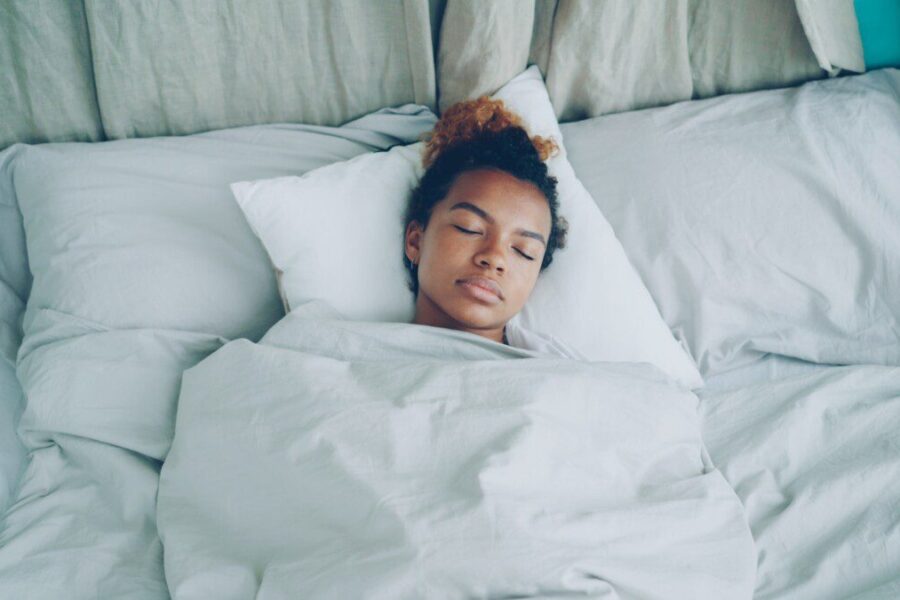 A young woman sleeping peacefully in a white bed.