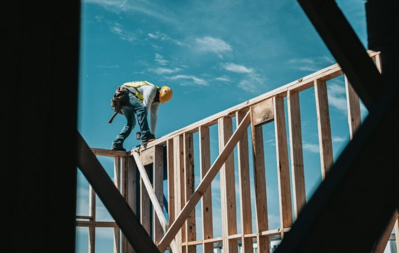 man in yellow shirt and blue denim jeans jumping on brown wooden railings under blue and