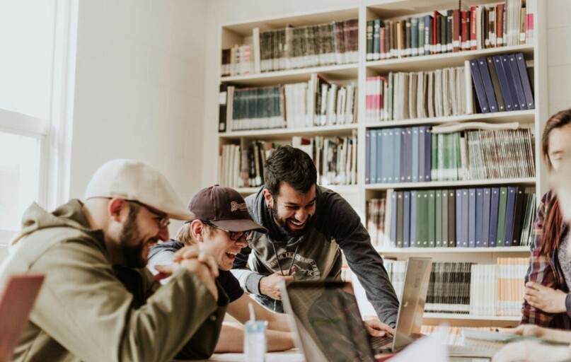 three men laughing while looking in the laptop inside room