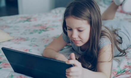 A girl is using a tablet on her bed.