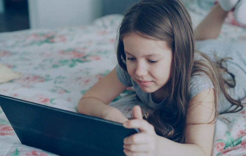 A girl is using a tablet on her bed.