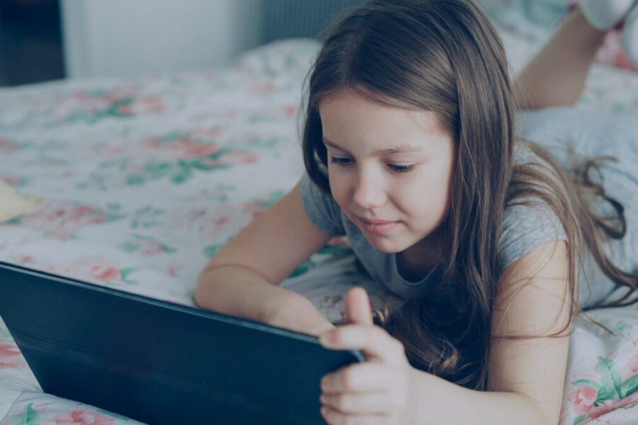 A girl is using a tablet on her bed.