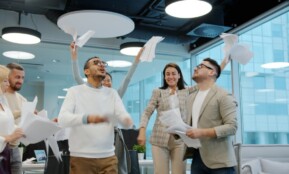 Diverse team celebrating by throwing papers in office