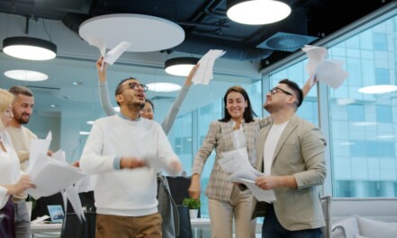 Diverse team celebrating by throwing papers in office