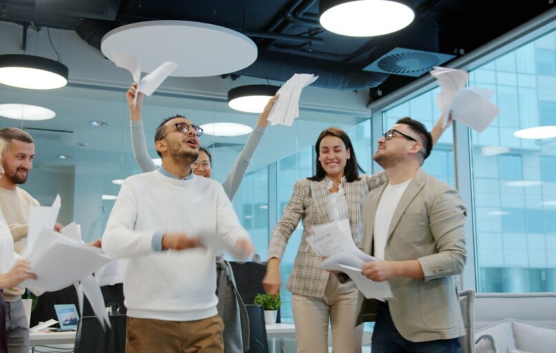 Diverse team celebrating by throwing papers in office