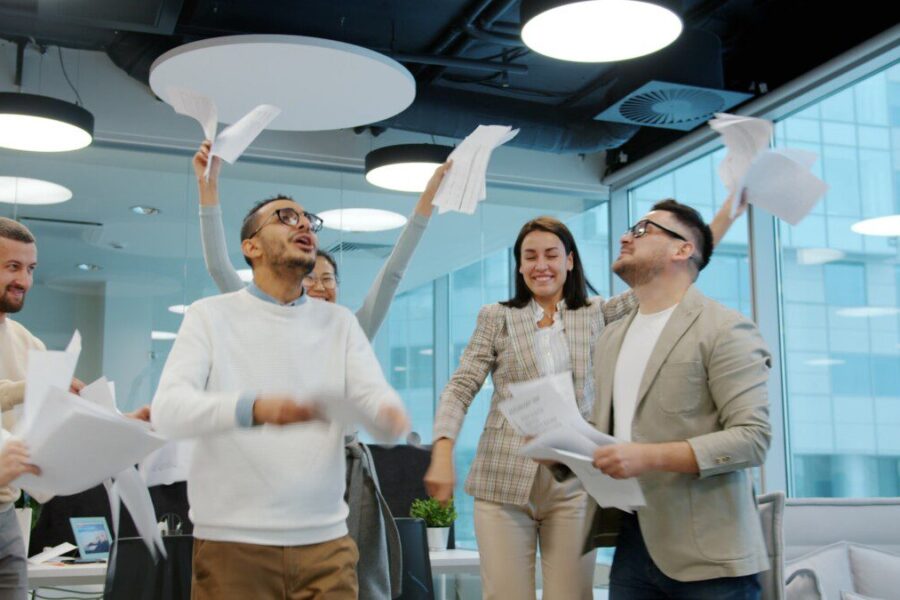 Diverse team celebrating by throwing papers in office