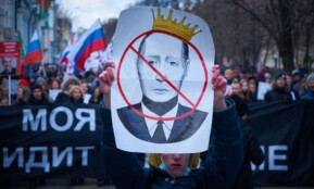 man in blue jacket holding white and red bird print banner