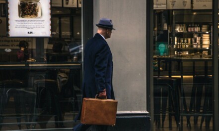 man in black suit jacket and blue hat standing in front of store