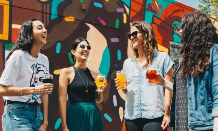 four women holding drinks while laughing together during daytime