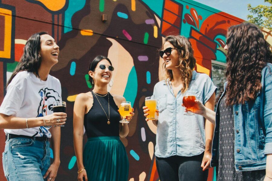 four women holding drinks while laughing together during daytime