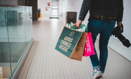 person walking while carrying a camera and paper bags