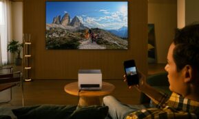 Man uses projector to display mountain landscape on wall.