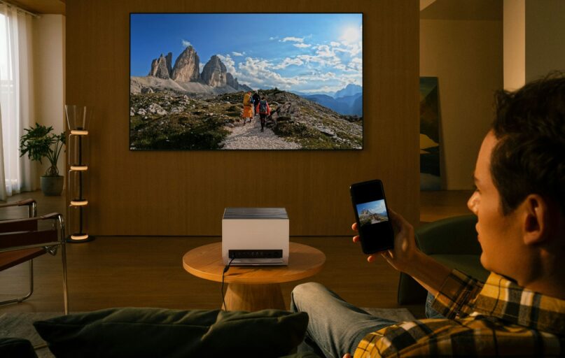 Man uses projector to display mountain landscape on wall.