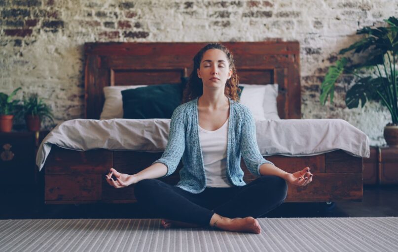 Woman meditating peacefully in a bedroom.