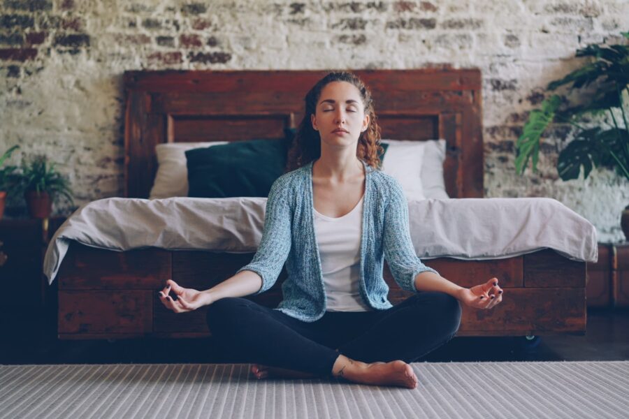 Woman meditating peacefully in a bedroom.