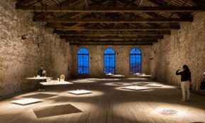 a person taking a picture of a person sitting at a table in a large room with windows