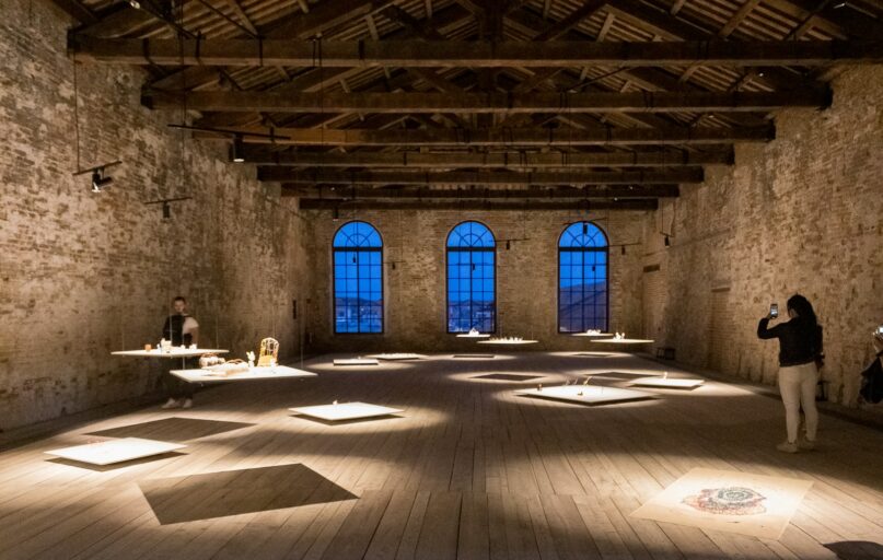a person taking a picture of a person sitting at a table in a large room with windows