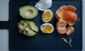 Avocado, egg, and mandarin orange ingredients on a board.