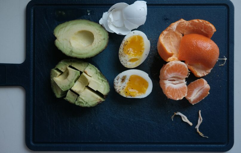 Avocado, egg, and mandarin orange ingredients on a board.
