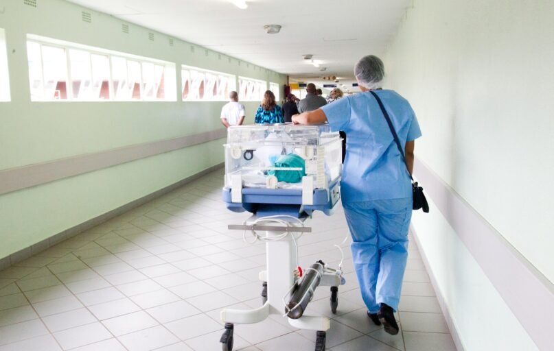 person walking on hallway in blue scrub suit near incubator