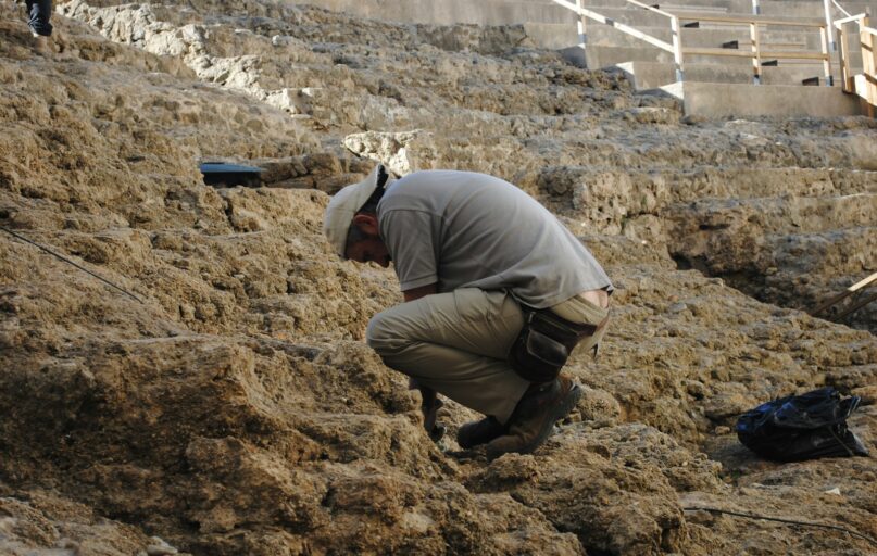 man in gray jacket and brown pants sitting on brown rock during daytime