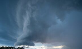 a very large cloud in the sky over a field