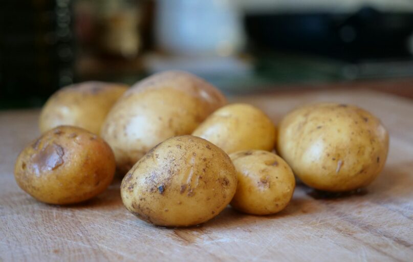 Several raw potatoes resting on a wooden surface