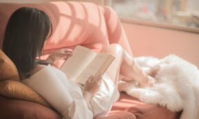 woman holding book sitting on pink fabric sofa