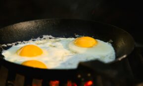 Three eggs frying in a black skillet over flames.