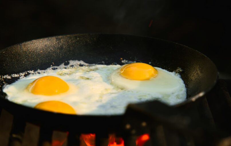 Three eggs frying in a black skillet over flames.