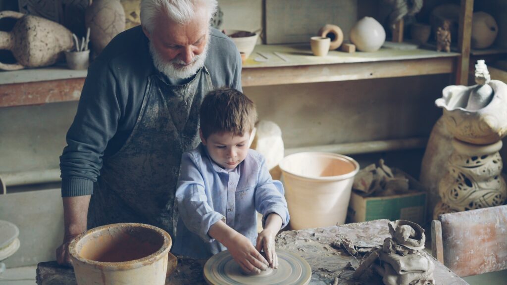 A grandfather teaches pottery to his grandson.