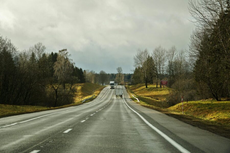 A straight highway with trucks amidst overcast skies and surrounding fields.