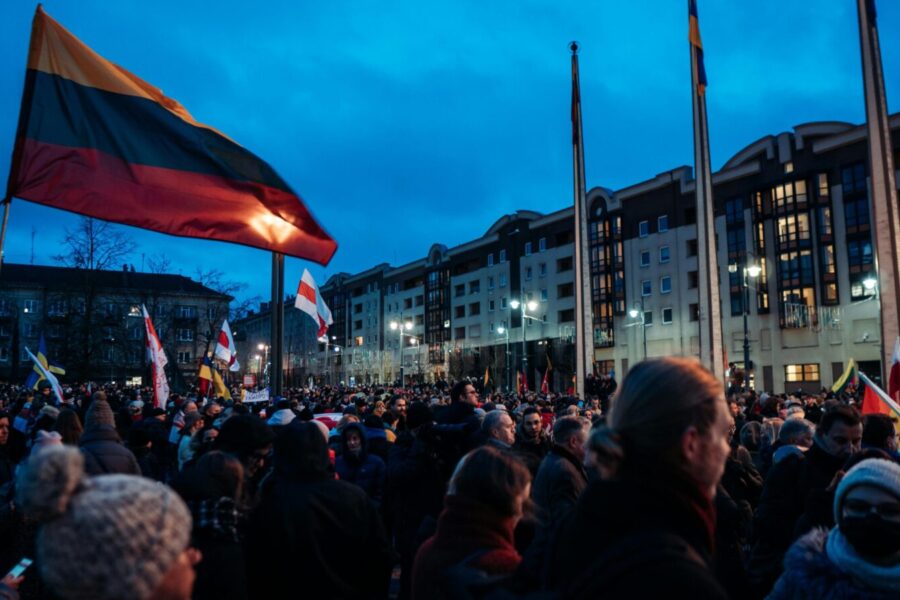 A large crowd gathers at dusk in Vilnius, Lithuania, waving flags during a peaceful protest.
