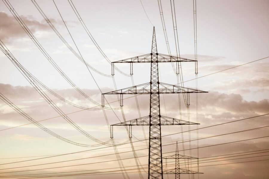 Silhouetted electricity pylons and power lines against a dramatic sky at sunset.