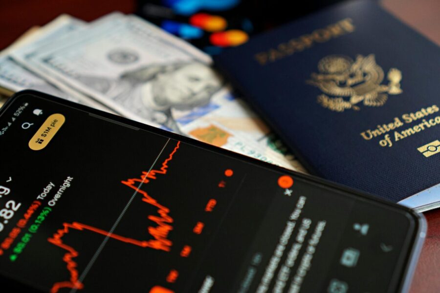 Close-up of smartphone with stock chart, cash, and US passport, symbolizing travel and finance.