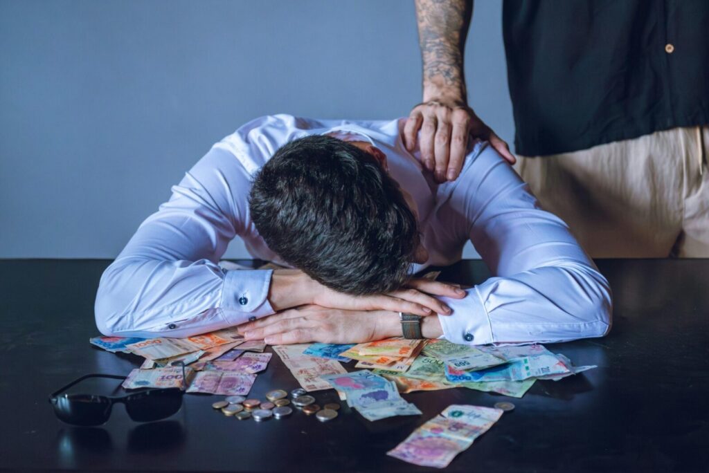 Depressed man surrounded by Argentine pesos represents financial stress and burnout.