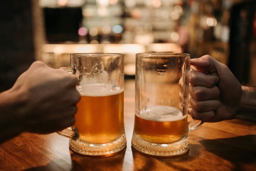 Close-up of two hands clinking beer mugs in a cozy bar atmosphere.