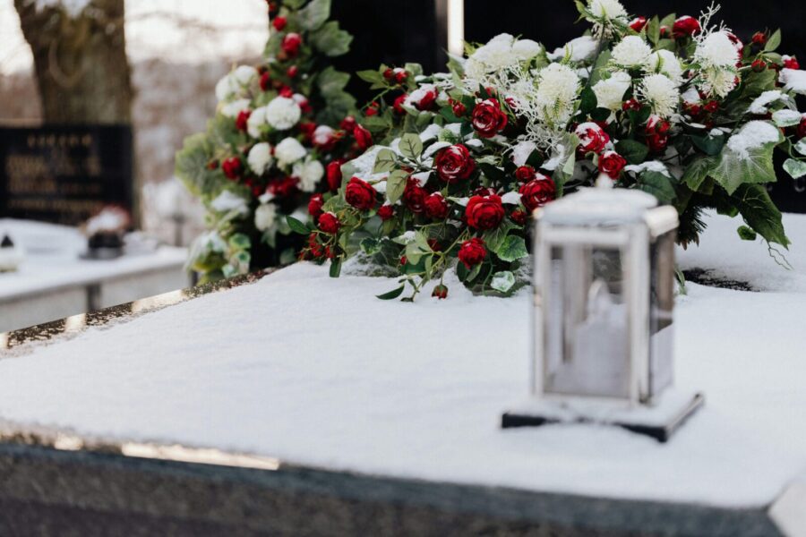 Grave adorned with roses and chrysanthemums in winter snow, evoking solemnity and remembrance.