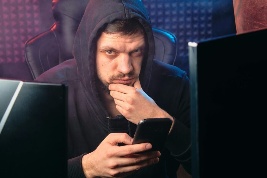 A man in a black hoodie contemplating while using a smartphone, surrounded by digital screens.
