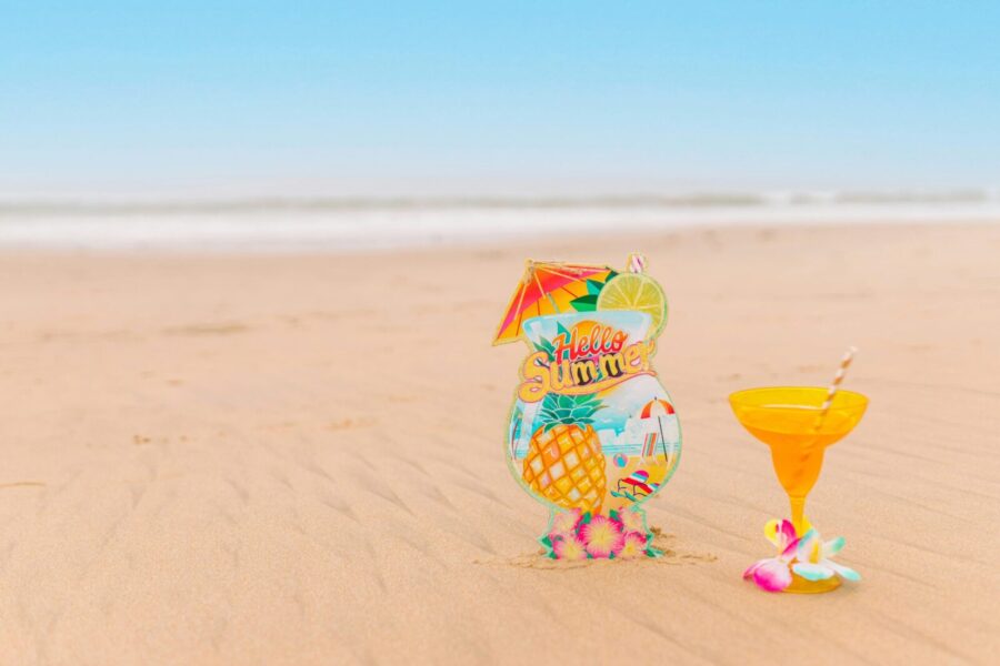A vibrant beach scene featuring a 'Hello Summer' sign and a margarita glass on sandy shores.