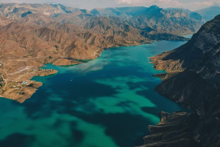Stunning aerial view showcasing a turquoise lake surrounded by rugged brown mountains on a clear day.